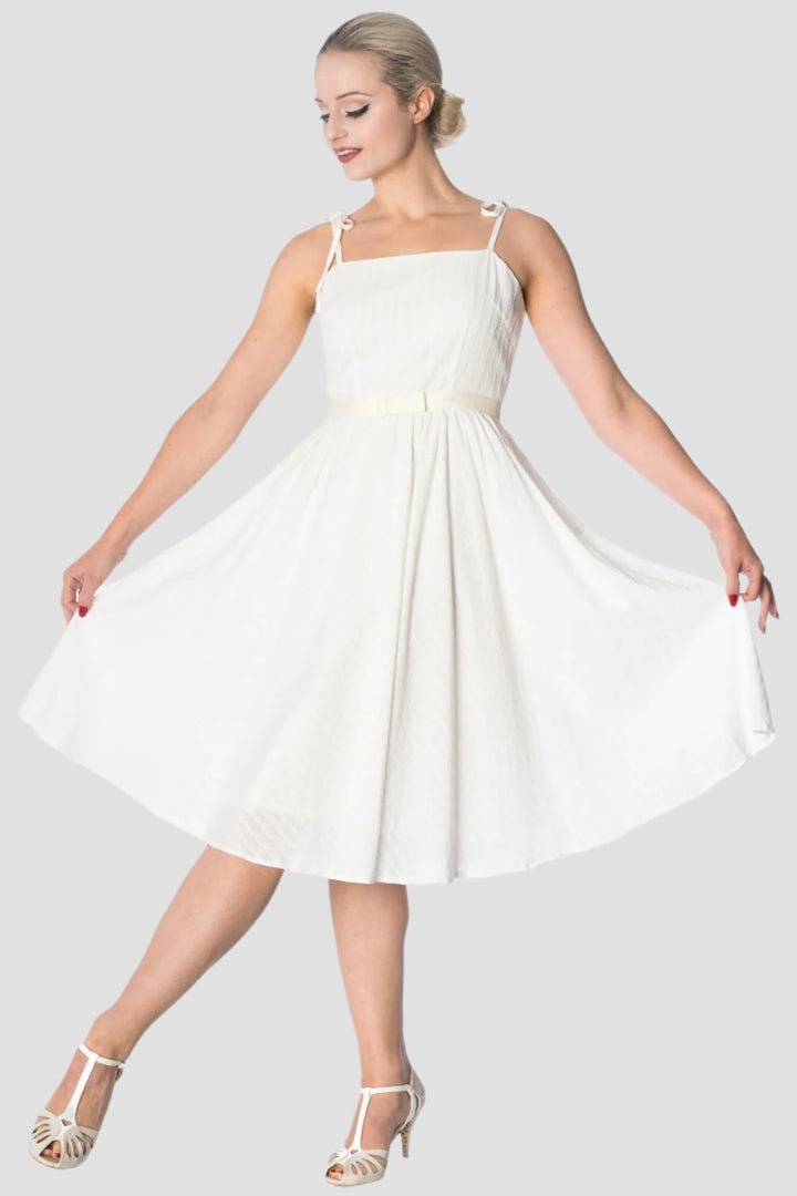 Woman in elegant white strappy sundress, twirling to showcase the flowing skirt and flattering silhouette. Perfect for any occasion.