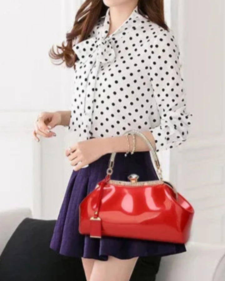 Woman in polka dot blouse holding a red patent handbag, showcasing a stylish and elegant accessory.