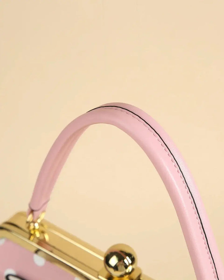 Close-up of the pink handle of a vintage-inspired polka dot handbag with a gold kiss-lock clasp.