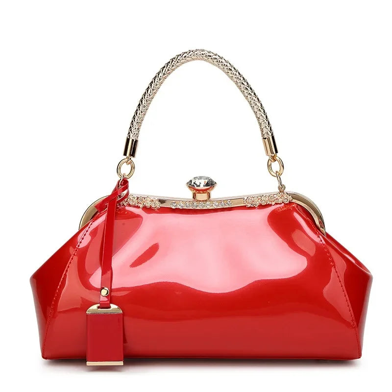 Red patent women's handbag with a sleek design and rhinestone lock, perfect for stylish occasions.