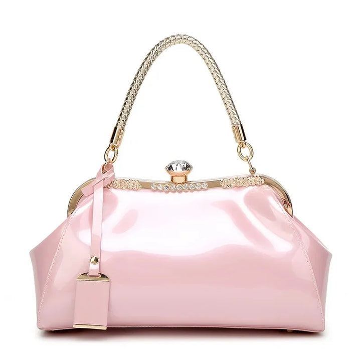 Stylish pink patent women's handbag with rhinestone clip lock and chain handle for modern elegance.