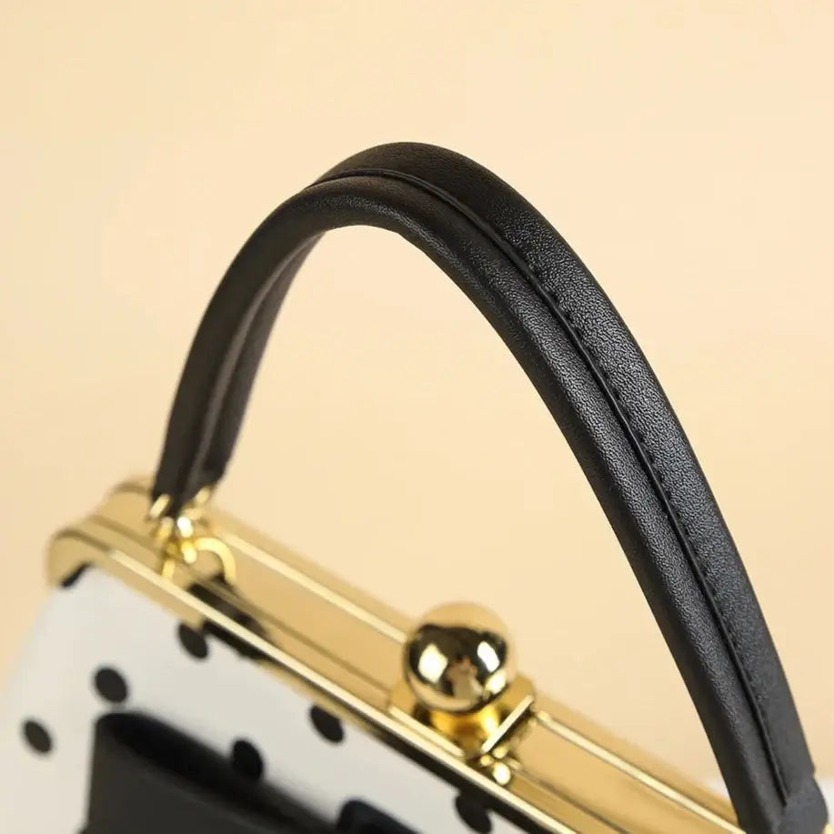 Close-up of the black handle on a vintage-style black and white polka dot handbag with a classic kiss-lock closure.