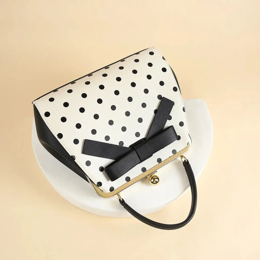 Black polka dot rockabilly handbag with bow detail, vintage-inspired design on a white plate.