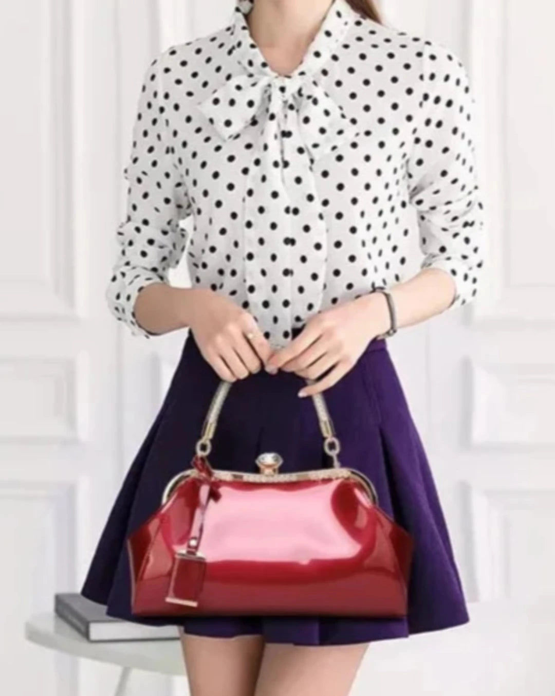 Burgundy patent handbag paired with a polka dot blouse and skirt, showcasing modern elegance and style.