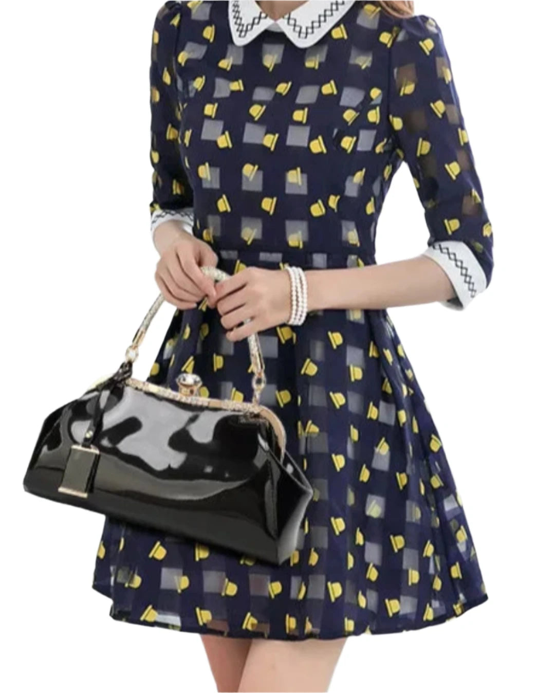 Woman in a navy dress with yellow patterns holding a stylish black patent handbag.