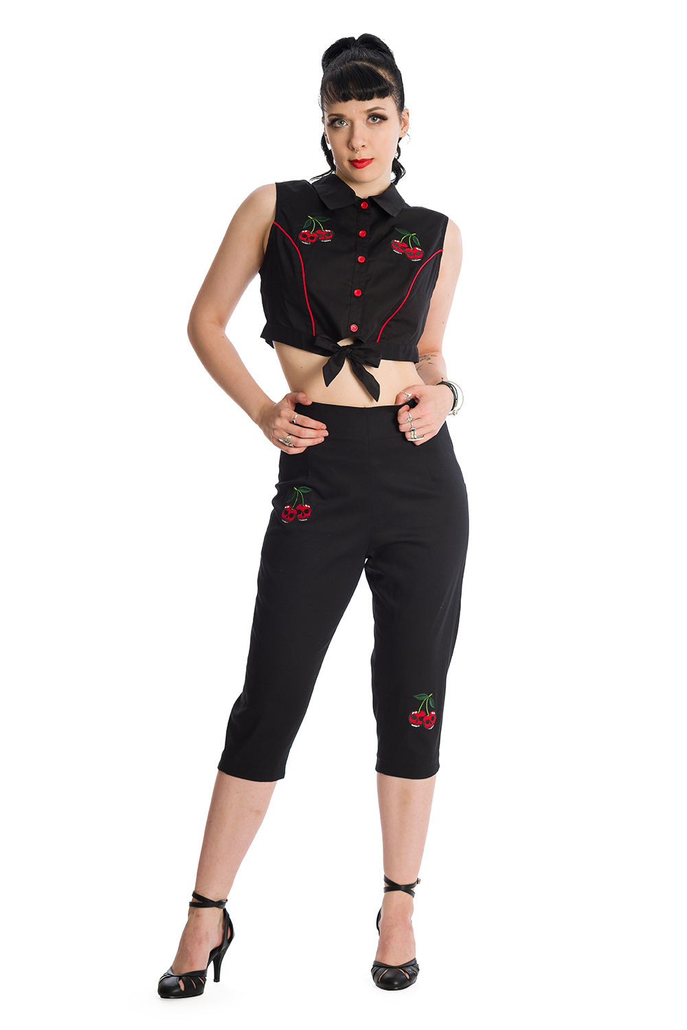 Model in high-waisted black pedal pushers with cherry skull embroidery and a cropped blouse, showcasing a rockabilly style.