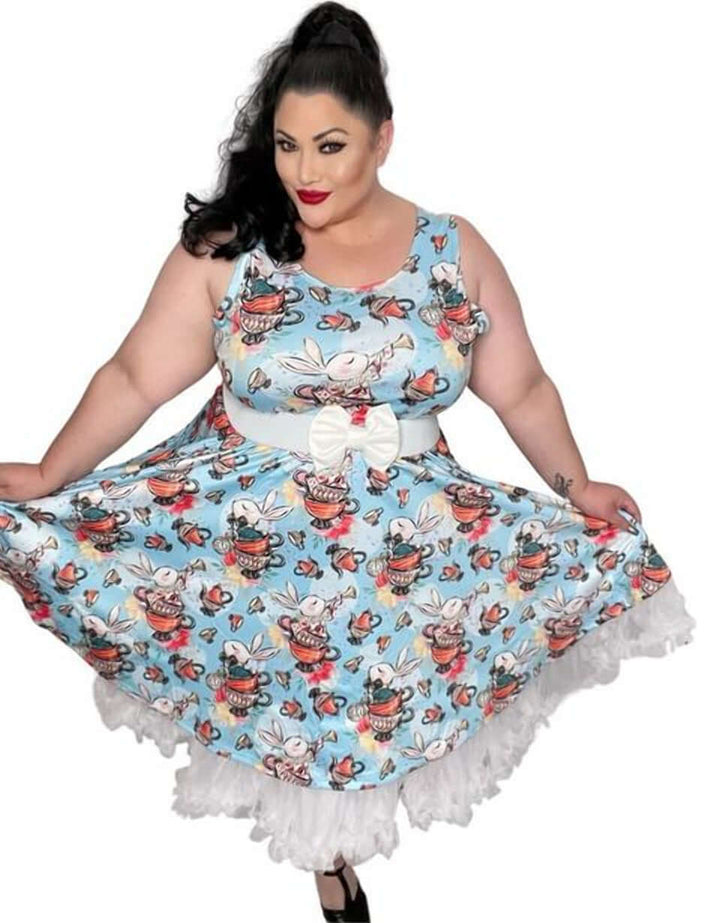 Plus-size model wearing a whimsical blue skater dress with vibrant tea party print and a white bow. Perfect for playful occasions.