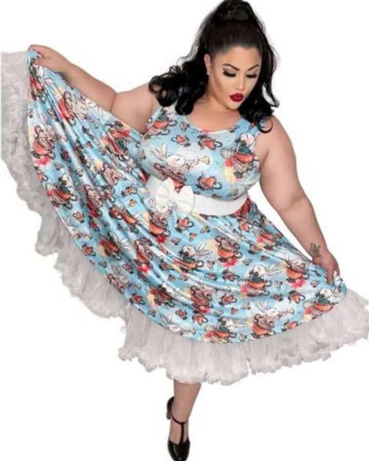 Model twirling in a blue skater dress with whimsical Alice in Wonderland print and white lace trim. Perfect for spring occasions.